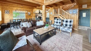 A log cabin interior with a dining area, a living room with a sofa and armchairs, a staircase, and a blue door. - Cozy Cabin Close to Lake Cascade w/ Hot Tub (Cascade)