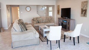 Ein Wohnzimmer mit einer Couch, zwei Sesseln, einem Couchtisch, einem Fernseher und einem Schrank.