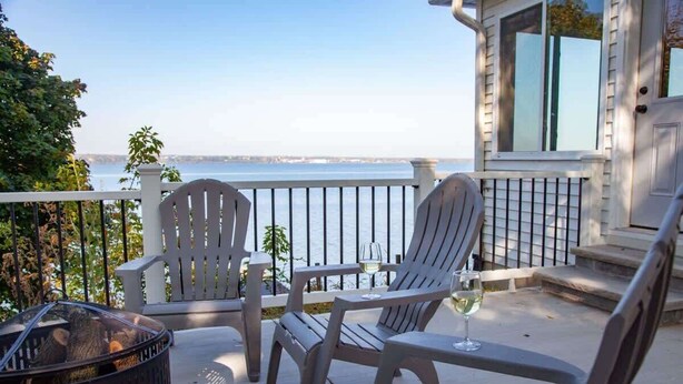 Ein Balkon mit Adirondack-Stühlen, einer Feuerstelle und einem Glas Wein.