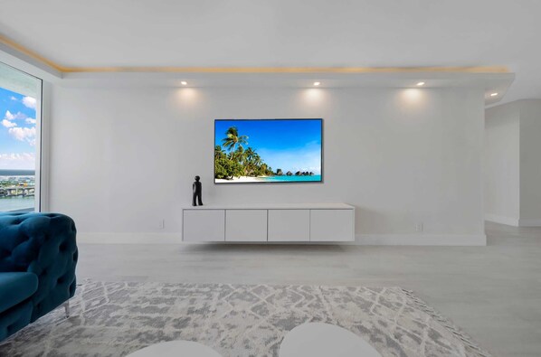A modern living room with a large flat-screen TV mounted on a white cabinet, a blue sofa, and a patterned rug.