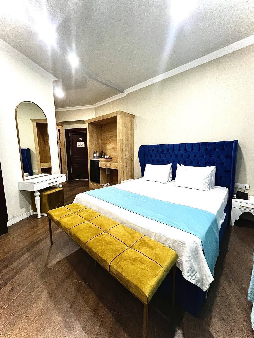 A bedroom with a bed, a bench, a mirror, a dresser, and a door.