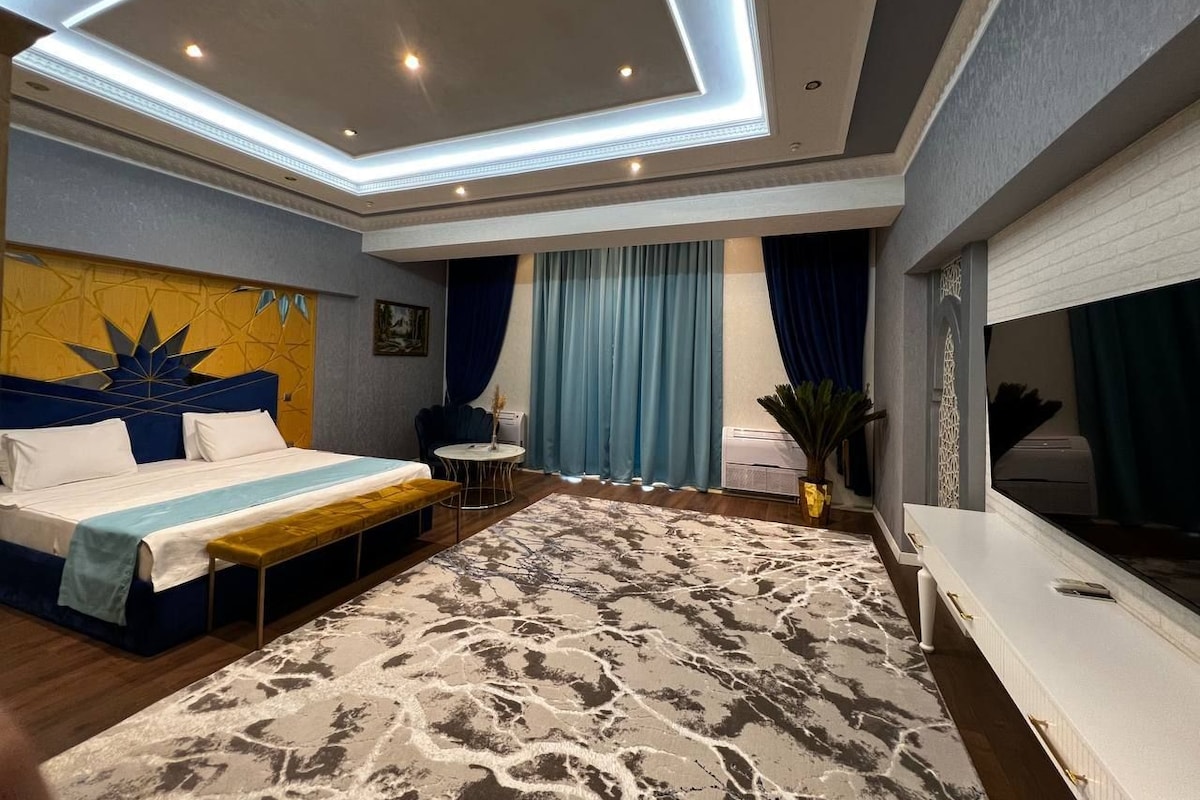 A modern hotel room with a bed, a desk, a chair, a TV, and a large window with curtains.