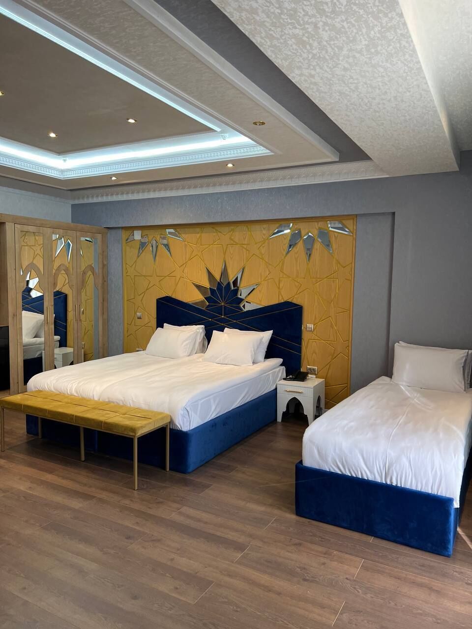 A hotel room with two beds, a bench, a mirror, and a decorative wall.