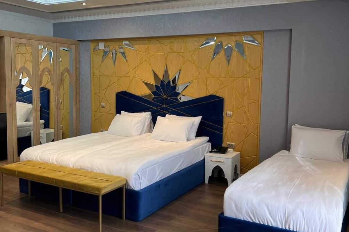 Hotellihuone, jossa on kaksi sänkyä, penkki, peili ja koristeellinen seinä.