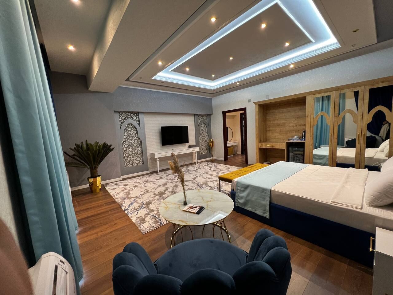 A modern hotel room with a bed, seating area, and a TV.