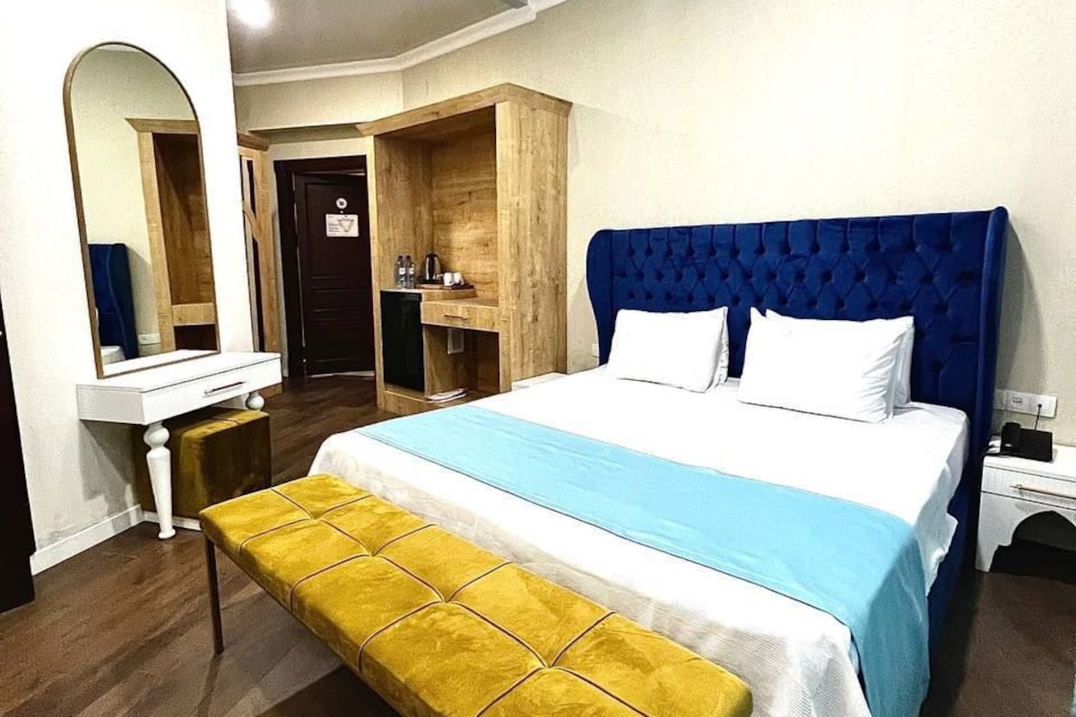 A bedroom with a bed, a bench, a mirror, a dresser, and a door.