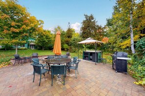 An outdoor patio with a round table and chairs, a grill, and a covered seating area.