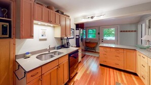 A kitchen with wooden cabinets, a sink, a dishwasher, and a window with a view of greenery. - Moon Path on Little Glen (Empire)