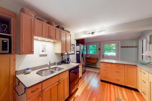 A kitchen with wooden cabinets, a sink, a dishwasher, and a window with a view of greenery. - Moon Path on Little Glen (Empire)
