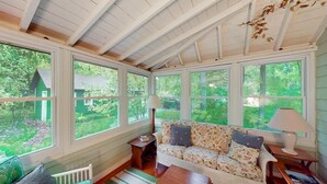 A cozy room with a sofa, a table, and a window overlooking a green landscape. - Moon Path on Little Glen (Empire)