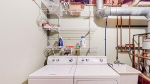 A laundry area with a front-loading washer and dryer, metal shelving with laundry supplies, and visible plumbing. - Moon Path on Little Glen (Empire)