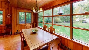 A wooden dining room with a large table and chairs, large windows with a view of a yard, and a chandelier. - Moon Path on Little Glen (Empire)