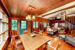 A spacious wooden cabin with a dining area, living room, and a staircase leading to an upper level.