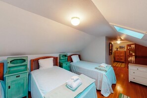 Une chambre avec deux lits, une lucarne, une commode en bois et une petite table avec une serviette.