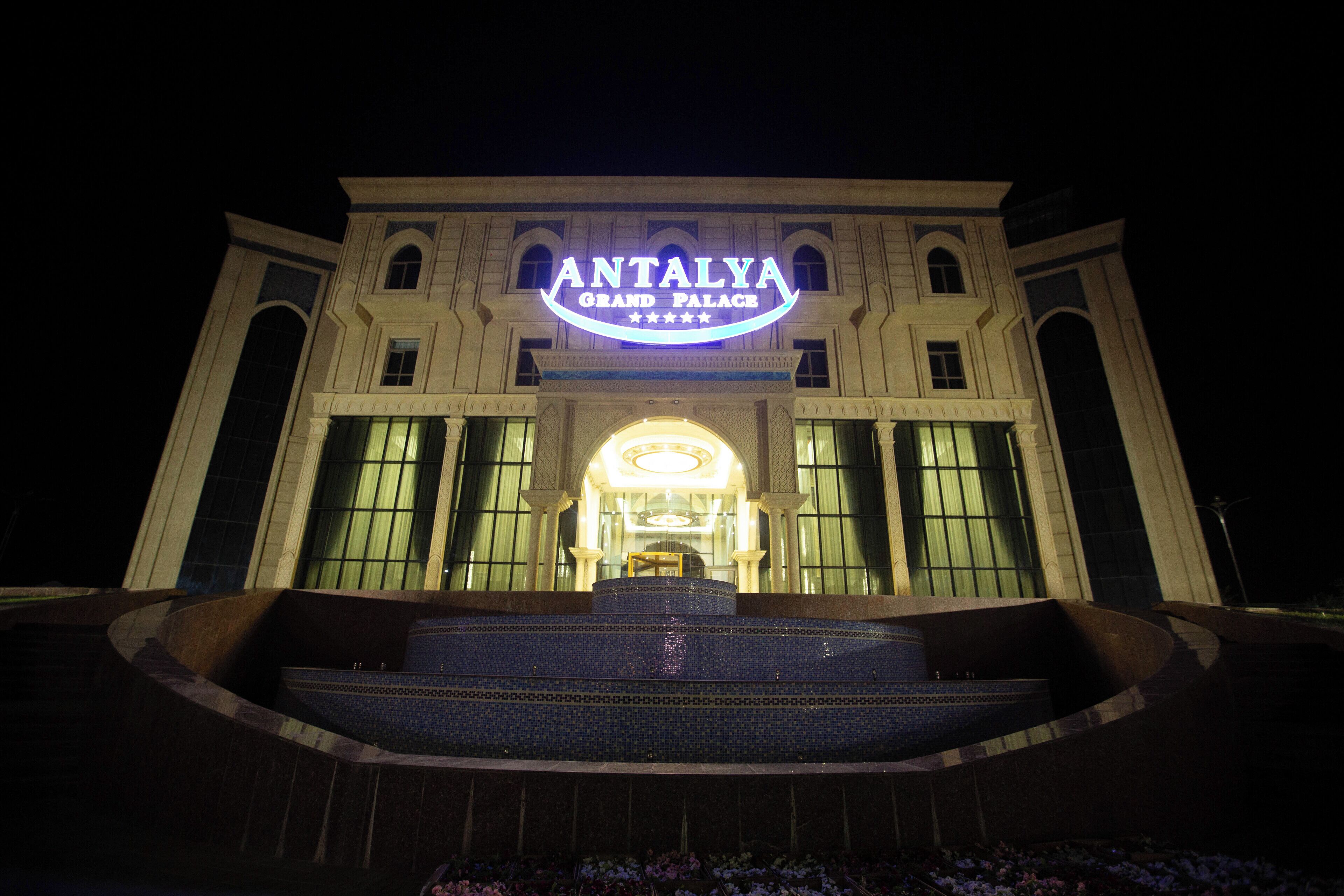 The exterior of the Antalya Grand Palace hotel with a prominent illuminated sign, large windows, and a grand entrance.