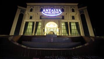 The exterior of the Antalya Grand Palace hotel with a prominent illuminated sign, large windows, and a grand entrance.