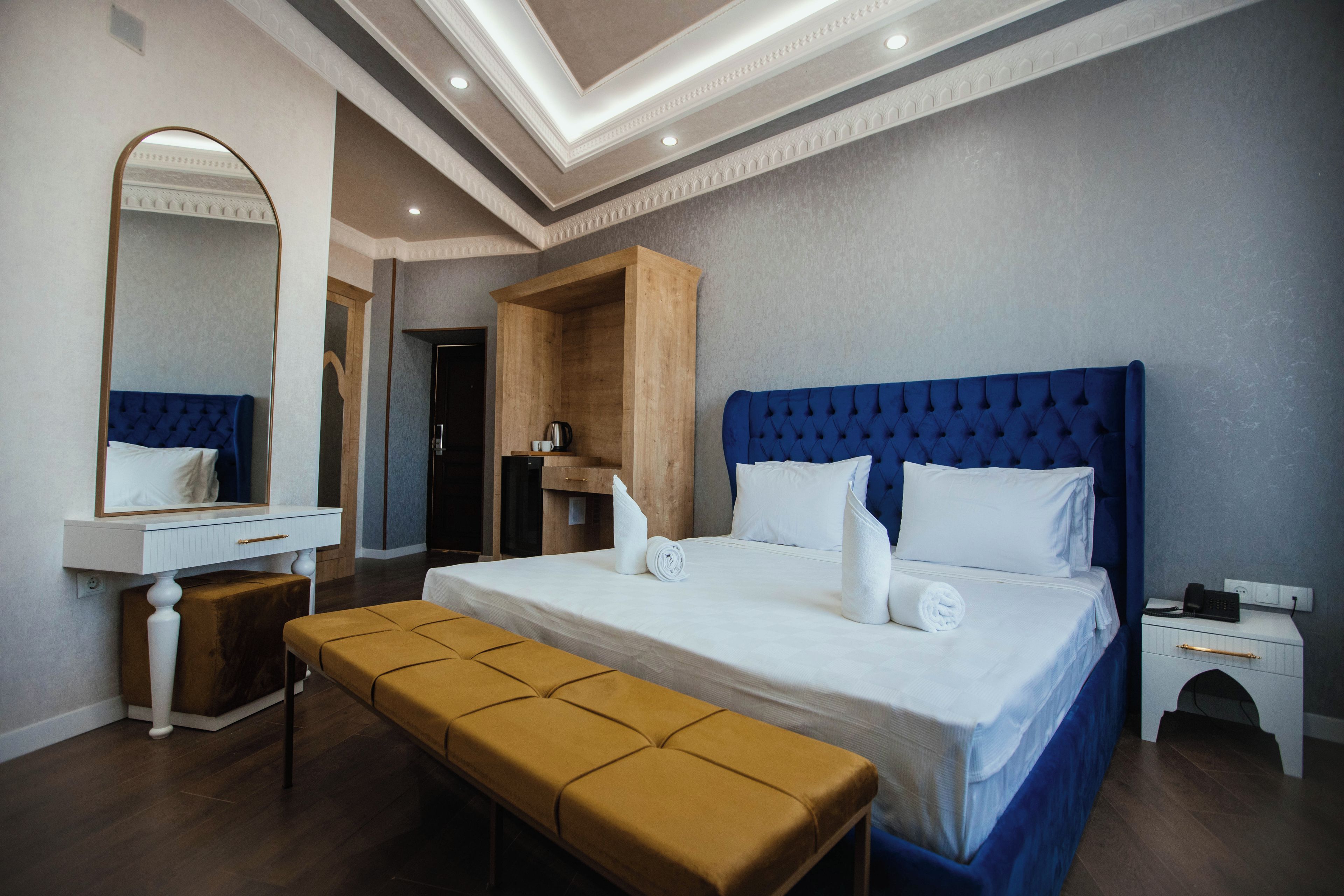 Una habitación de hotel con una cama grande, una mesita de noche, un banco, un espejo y un armario de madera.