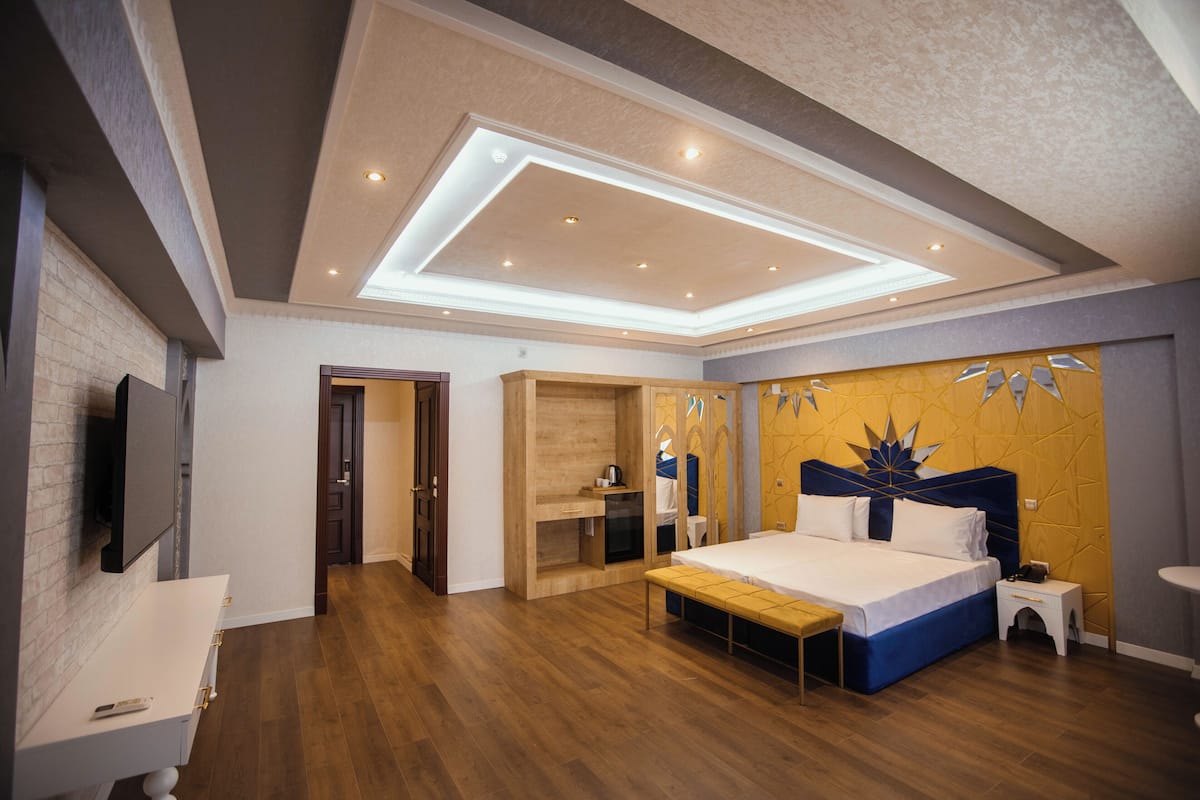 A modern bedroom with a large bed, a wooden bench, a built-in wardrobe, and a TV mounted on the wall.