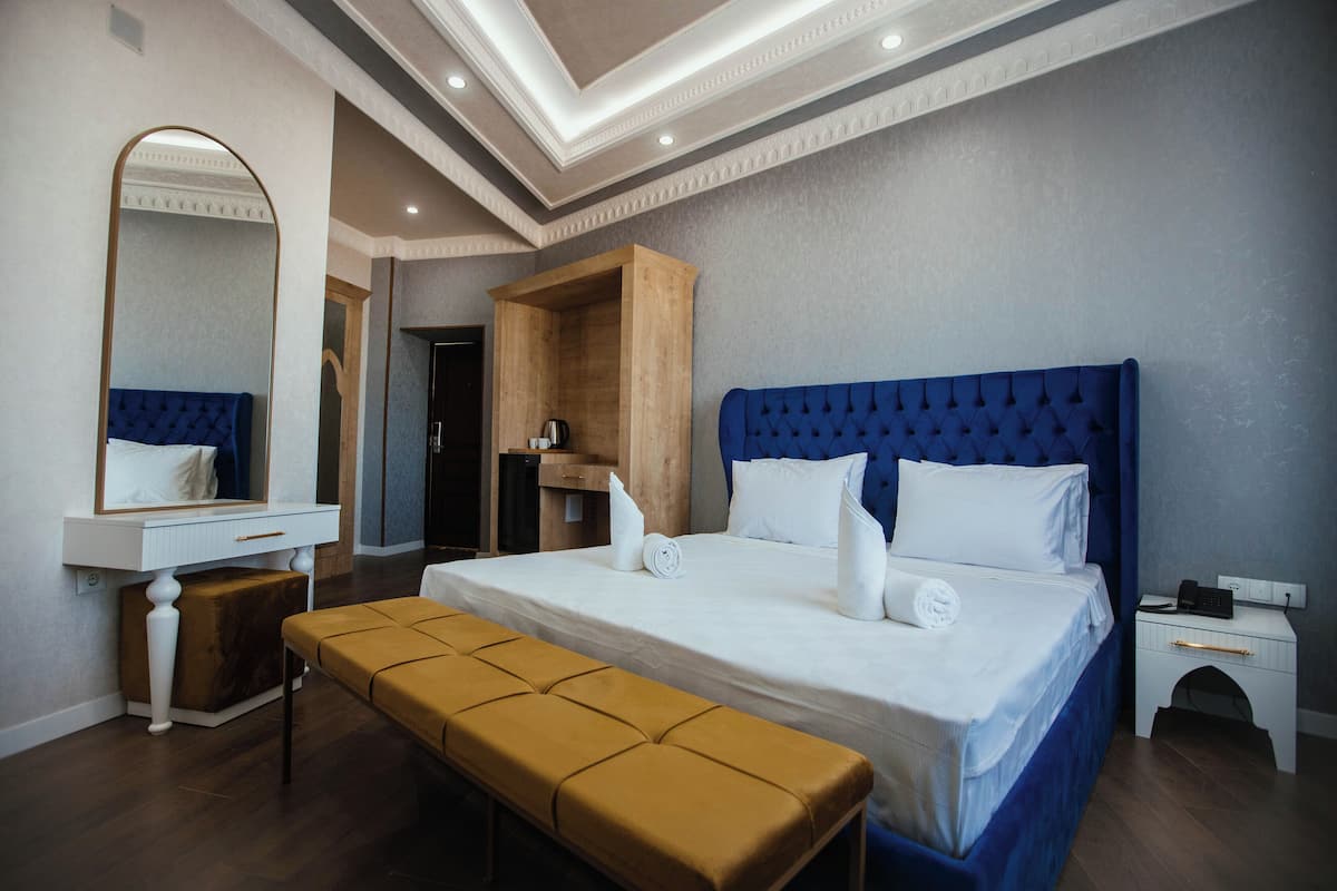 A modern hotel room with a large bed, a bench, a vanity with a mirror, and a wooden cabinet.