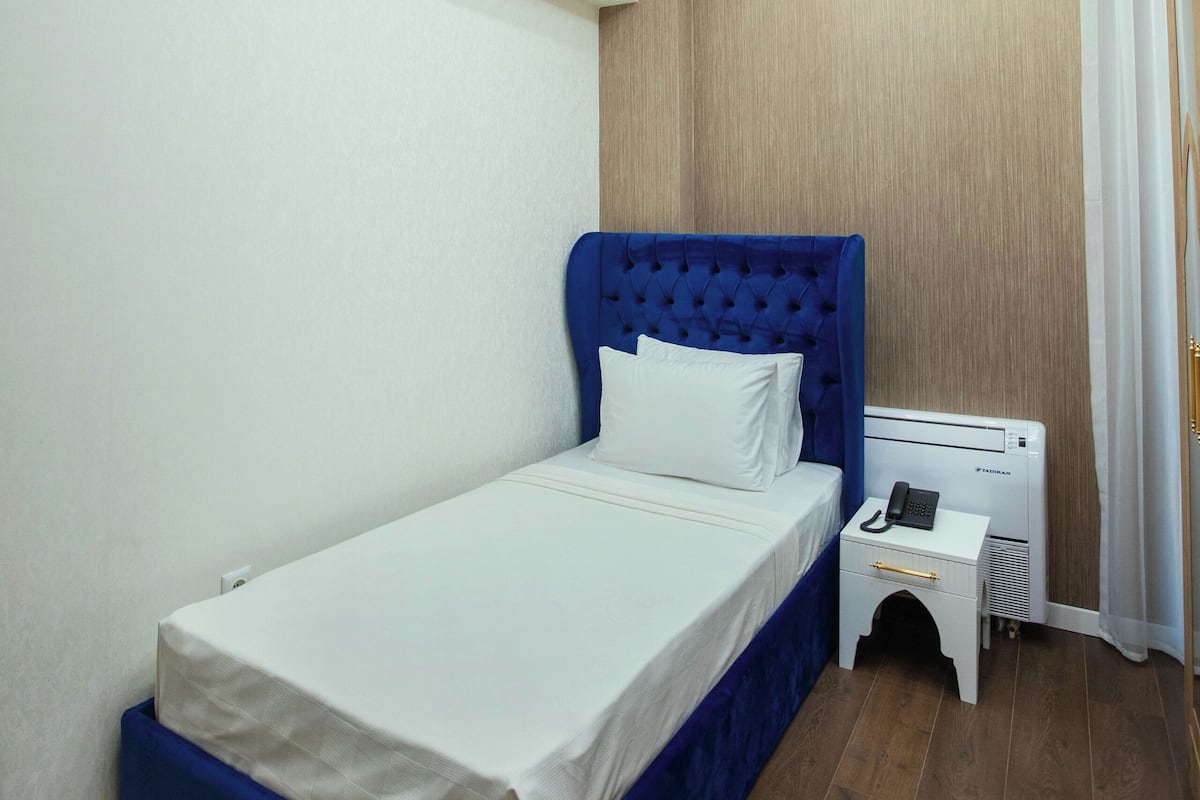 A bedroom with a single bed, a bedside table with a phone, and a wall-mounted heater.