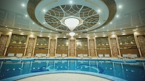 Una piscina interior amb un candelabrum central, dissenys ornamentals a la paret i diverses zones d'seure.