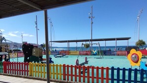 Ein Spielplatz direkt am Strand mit Schaukeln, Rutschen und einem eingezäunten Bereich.
