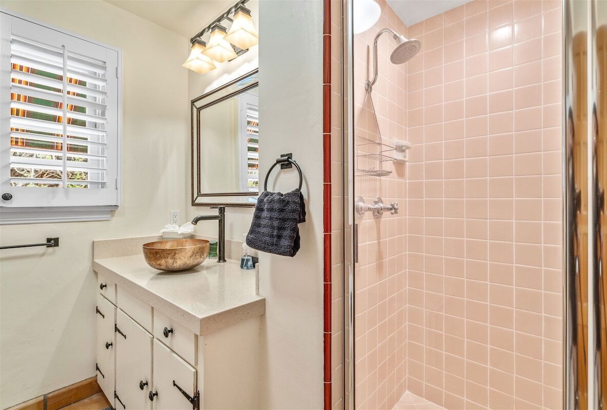 Casa de banho com toucador bege, um espelho grande, suporte para toalhas e um chuveiro com azulejos cor-de-rosa.