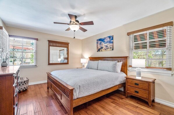 Une chambre à coucher avec un lit en bois, un ventilateur de plafond, une table de chevet, une commode et une fenêtre avec des stores.