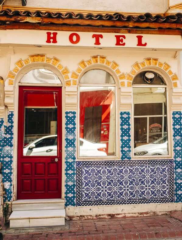 A hotel facade with a red door, three arched windows, and a tiled wall with a blue and white pattern. - KAYNARCA HOTEL (Iznik)