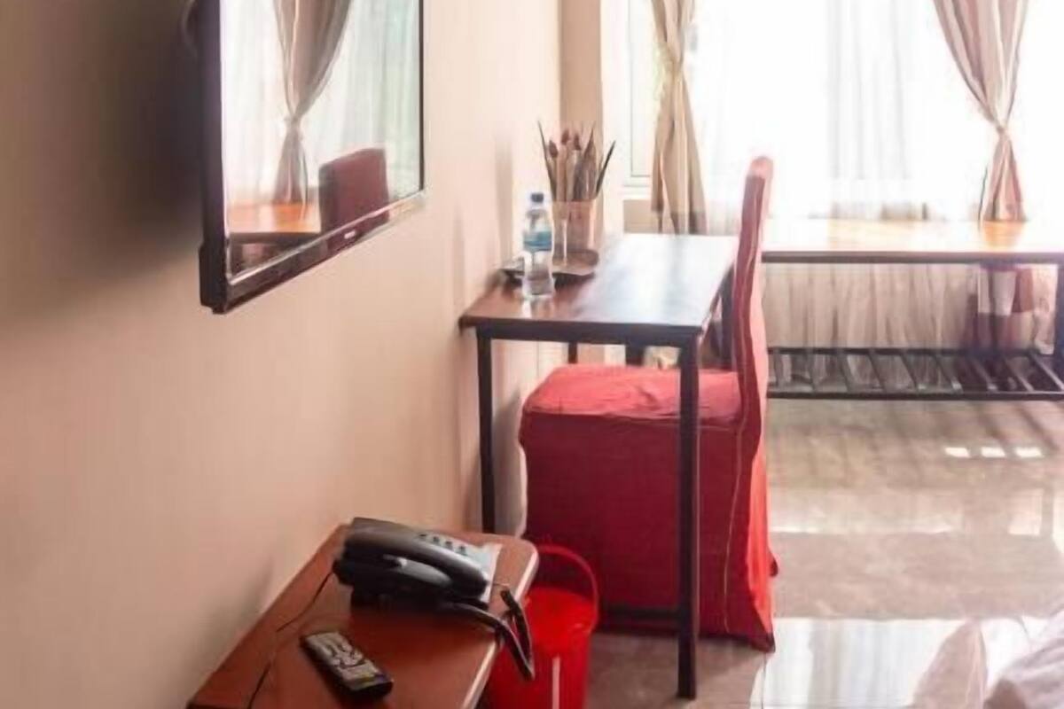 A hotel room with a bed, a desk with a chair, a mirror, and a window with curtains.