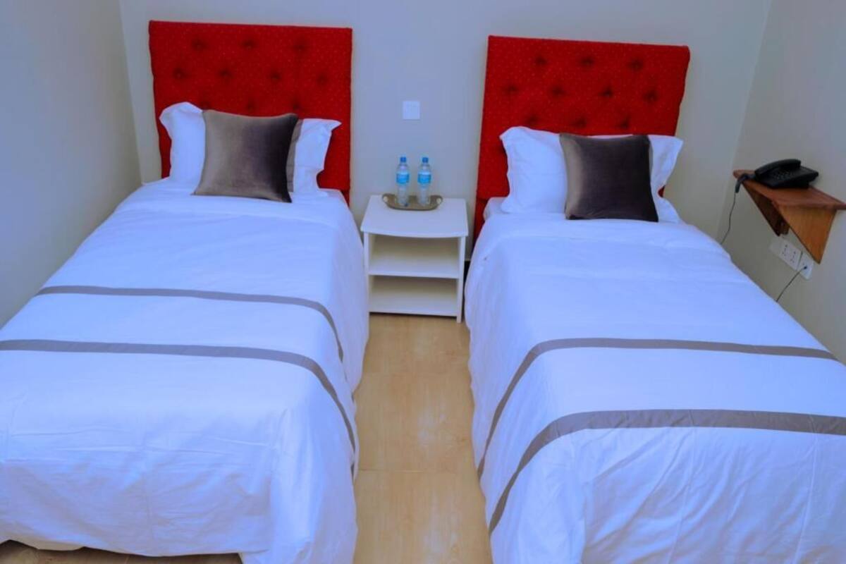 A hotel room with two beds, each with a red headboard, white bedding, and a small bedside table with water bottles.