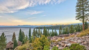 A lakeside view with rocky terrain, evergreen trees, and distant mountains.