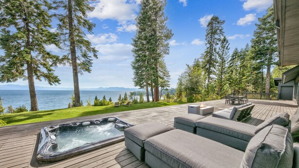 Eine Terrasse mit Whirlpool, einer grauen Couch und Blick auf Ozean und Berge.