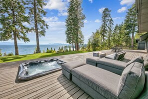 Une terrasse dotée d’un jacuzzi, d’un canapé gris et offrant une vue sur l’océan et les montagnes.