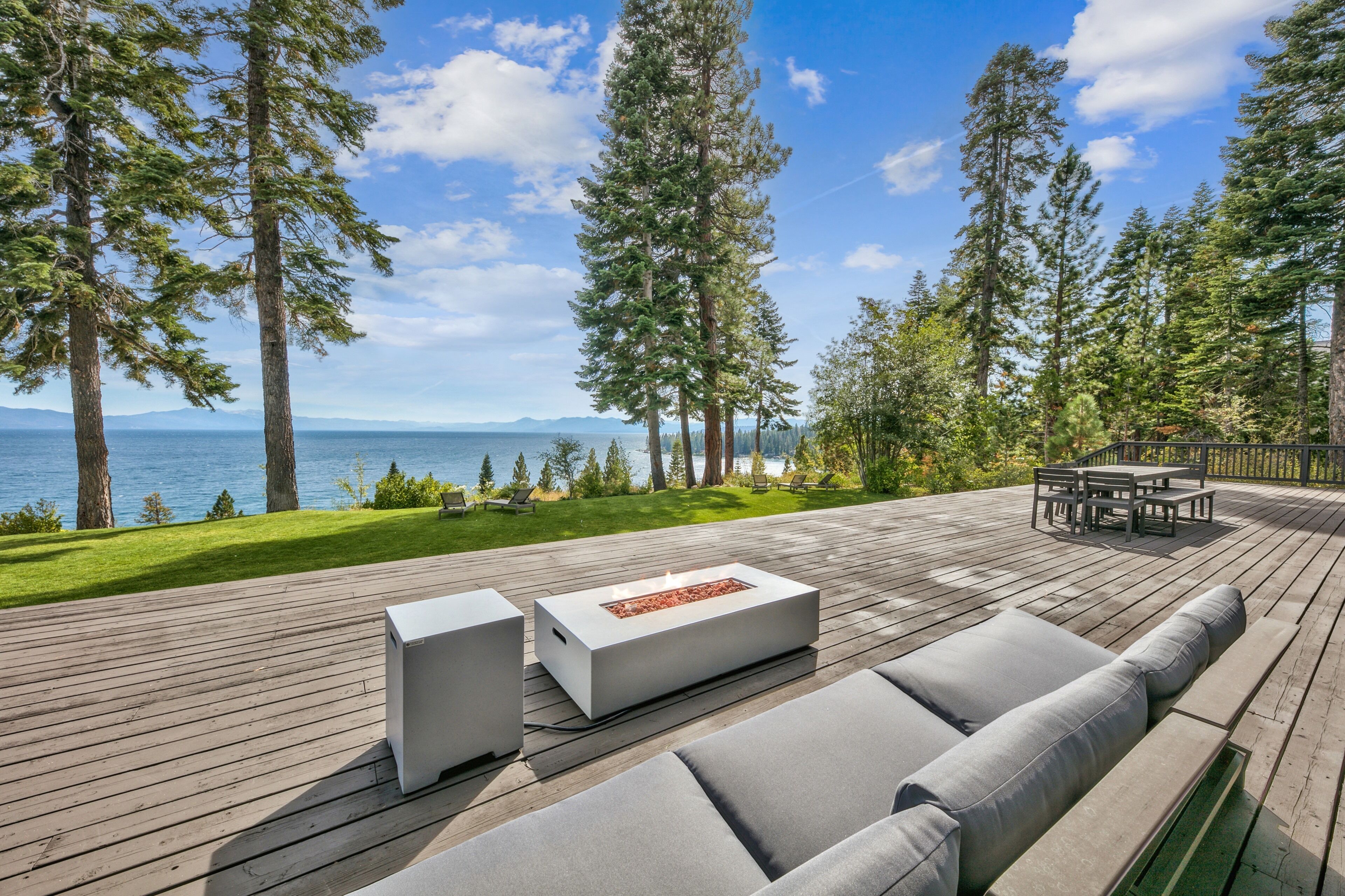 A deck with a fire pit, outdoor furniture, and a view of the ocean and mountains.