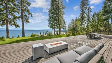 A deck with a fire pit, outdoor furniture, and a view of the ocean and mountains.