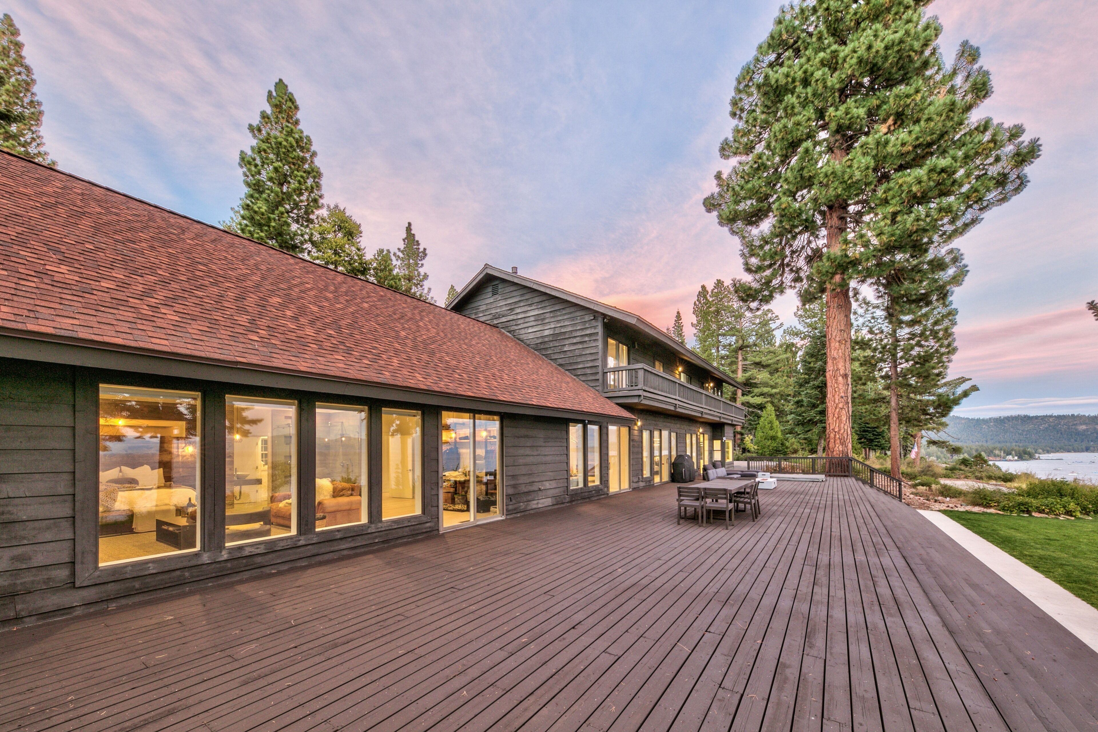 A modern house with a deck, large windows, and a view of a lake.
