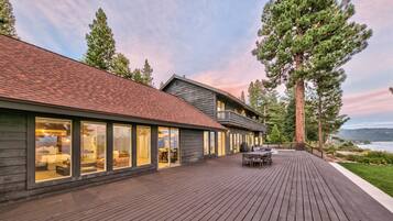 A modern house with a deck, large windows, and a view of a lake.