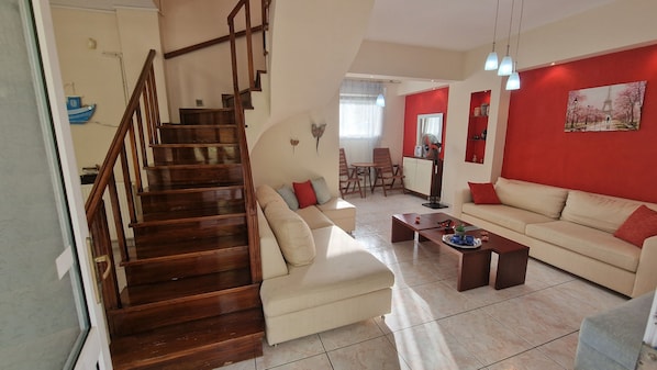 A living room with a wooden staircase, a sofa, a coffee table, and a dining area.