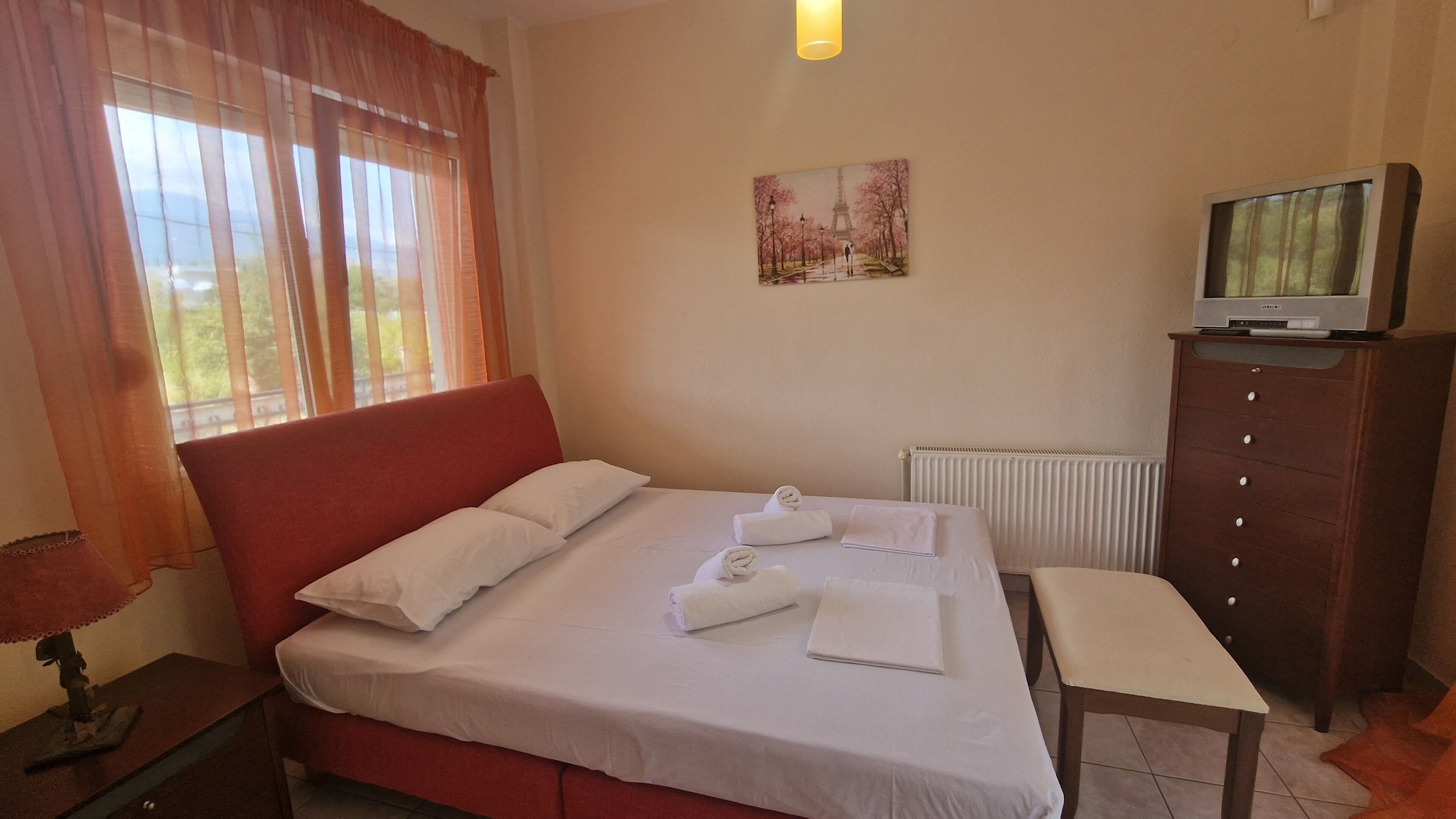 A hotel room with a bed, a bench, a TV, and a painting on the wall.