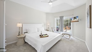 Une chambre avec un grand lit, un ventilateur de plafond, une fenêtre avec des rideaux et une vue sur l’extérieur.