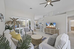 A spacious living room with a white sofa, a round coffee table, and a television on a cabinet. - Family friendly home w/ pool & steps to beach (Marco Island)