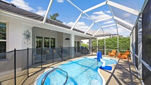 Un espace piscine couvert, doté d’une structure en verre, de chaises longues et d’un petit jacuzzi.