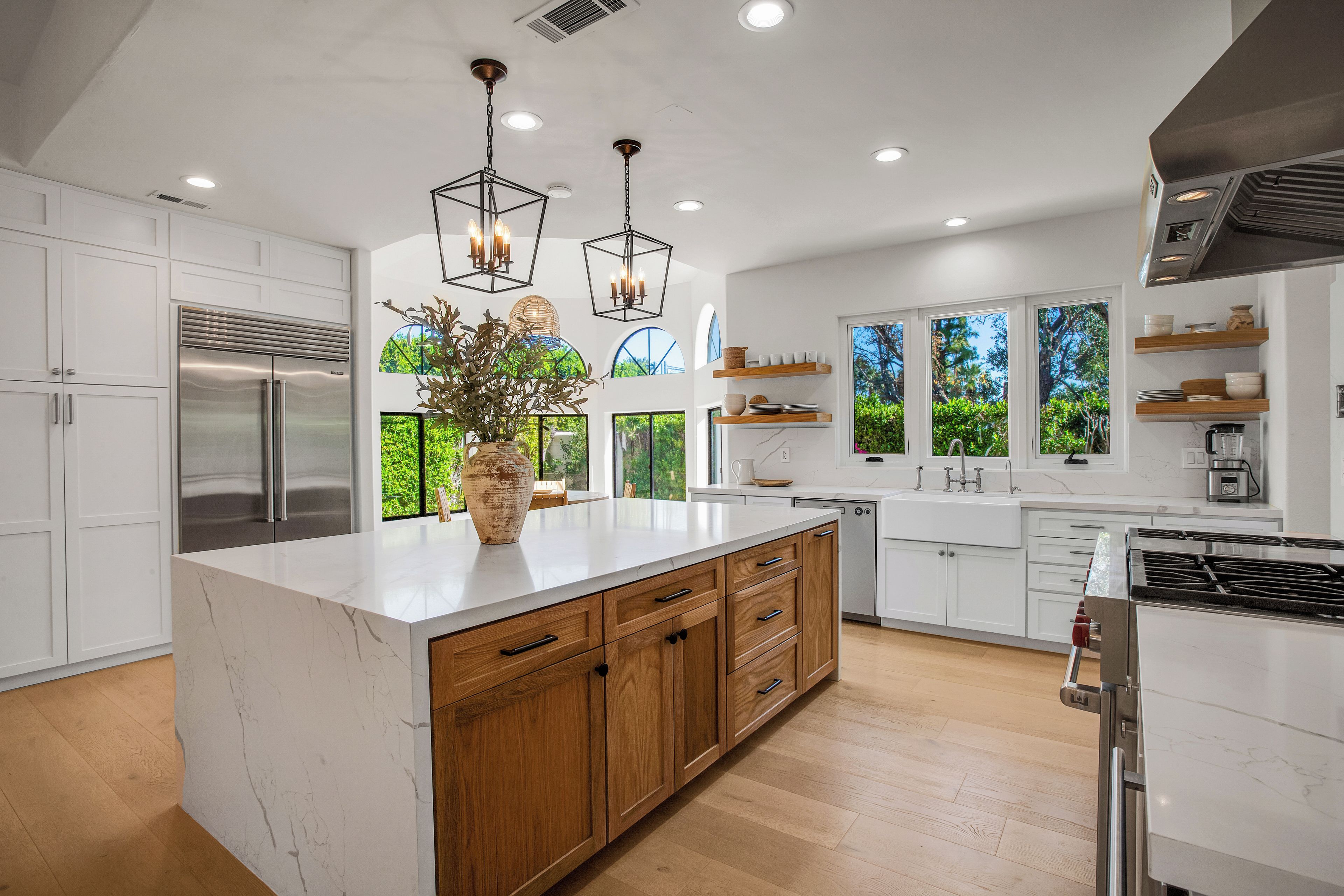 A modern kitchen with white cabinetry, a marble island, wooden lower cabinets, and pendant lighting.