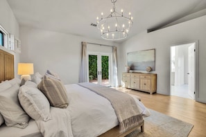 A bedroom with a large bed, a chandelier, a wooden cabinet, and a painting on the wall.