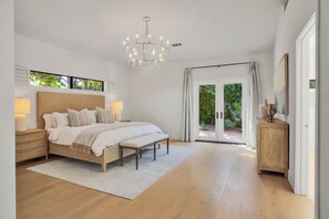Ein Schlafzimmer mit einem großen Bett, Nachttischlampen, einer Kandelaber, Blick durch eine Glastür und einem Holzkasten.