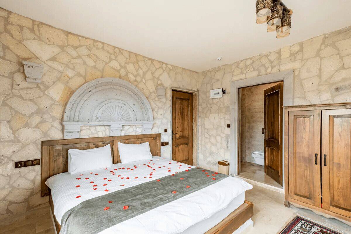 A bedroom with a stone wall, a bed with white bedding, a wooden headboard, and a wooden wardrobe.