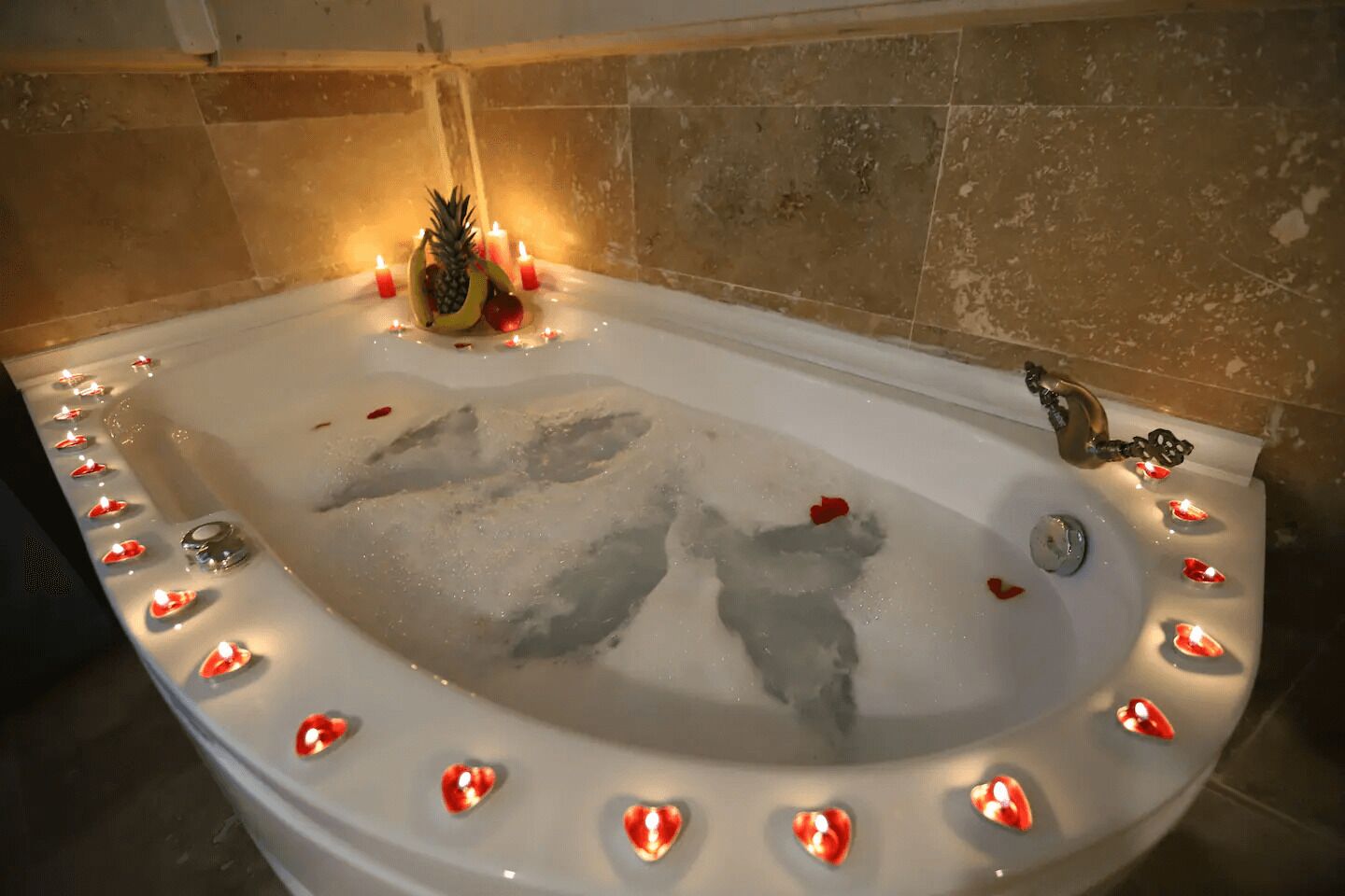 Une baignoire ornée de bougies en forme de cœur disposées sur le bord, et un ananas posé sur le bord.
