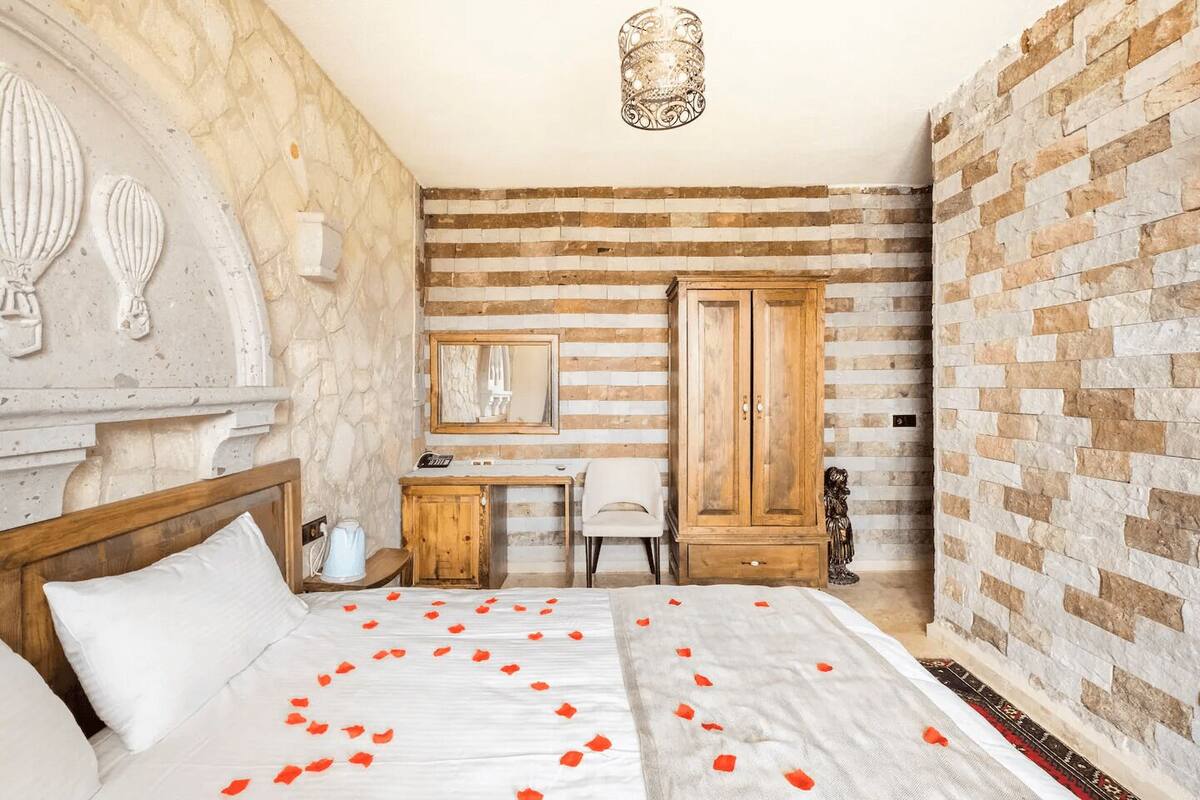 A bedroom with a bed, a desk, a wardrobe, and a stone wall.