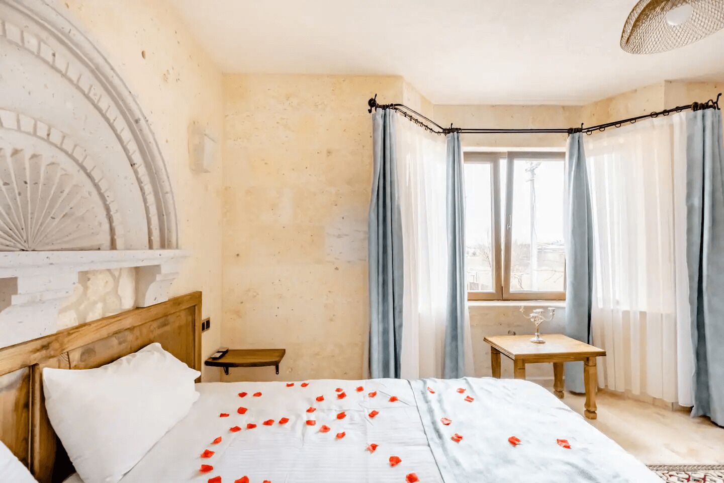 A hotel room with a bed, a small table with a glass, and a view of the city through large windows.